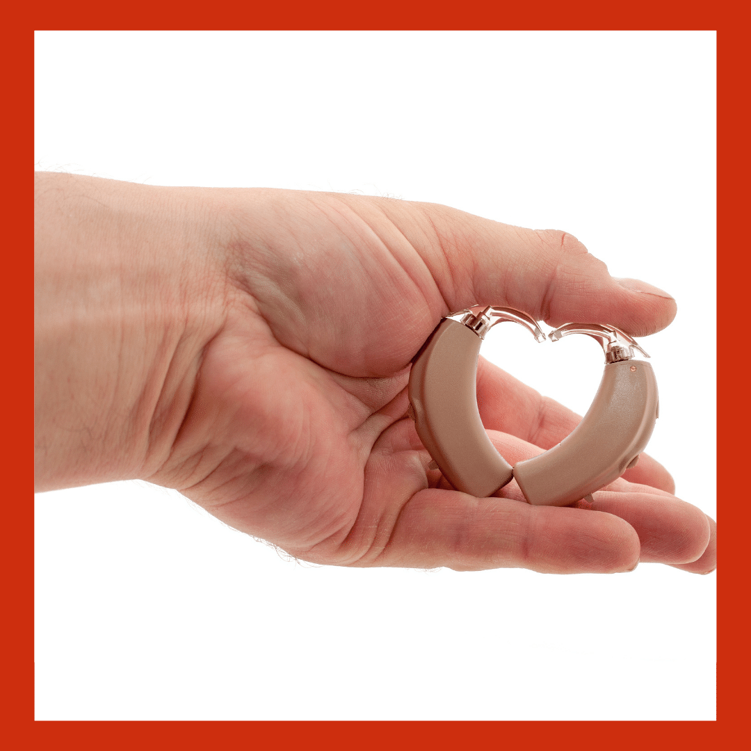 A hand holding two hearing aids in the shape of a heart 