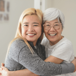 Two Asian women hugging. woman on the left has yellow hair, the woman on the right has white hair.
