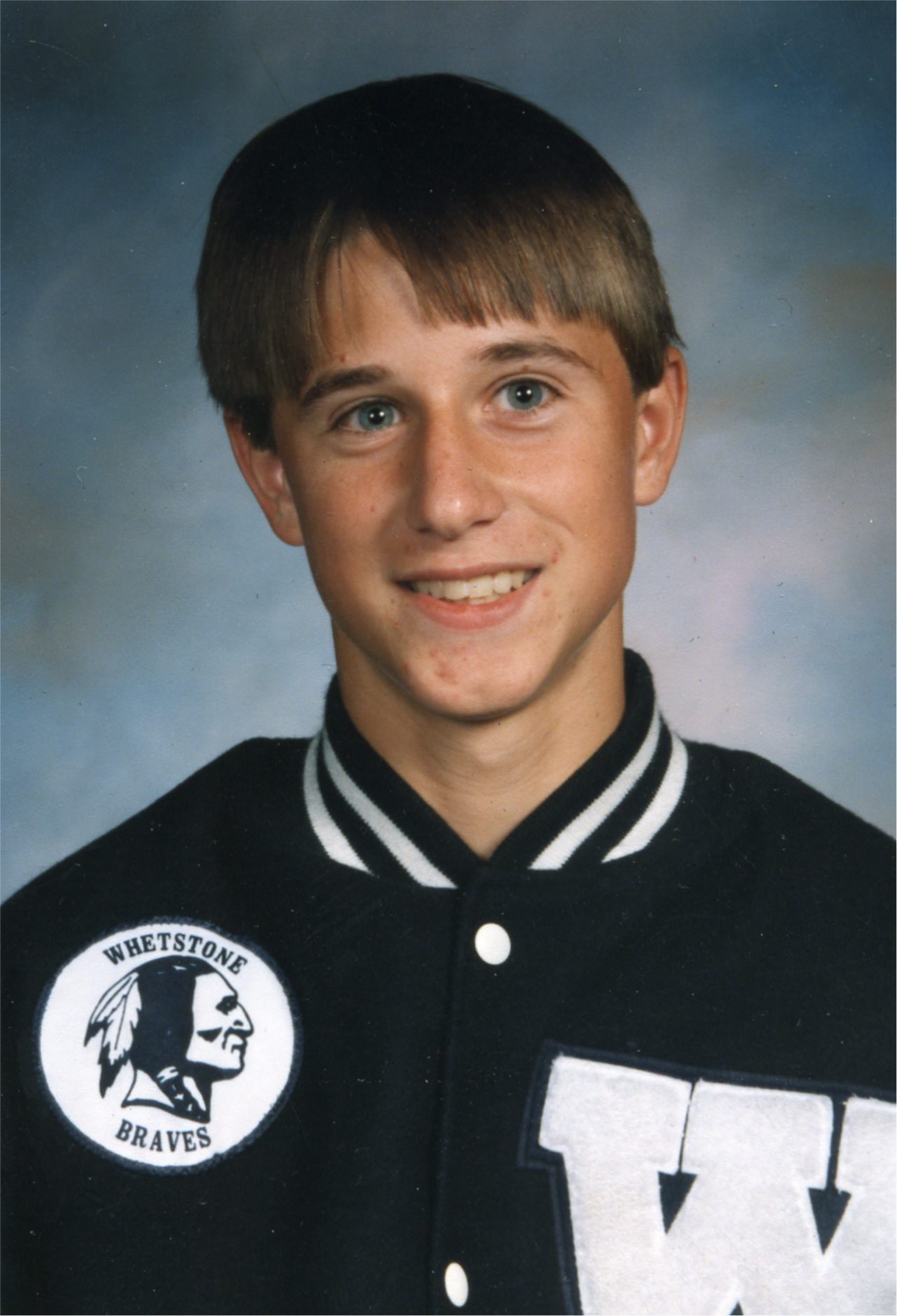 Caucasian boy with a blue and white letterman jacket on.  Grey and blue background.  